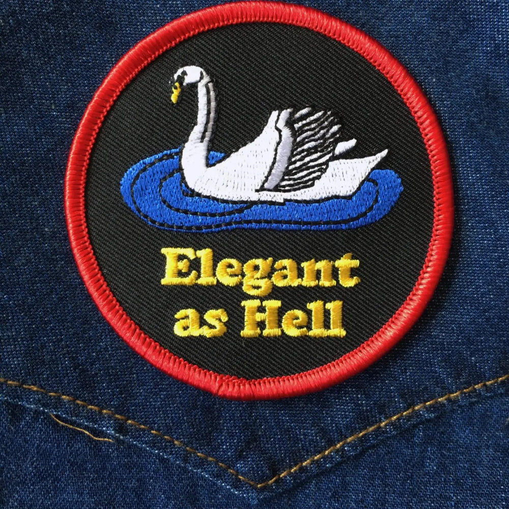 Black patch with red boarder, a white swan, and yellow lettering saying "elegant as hell"