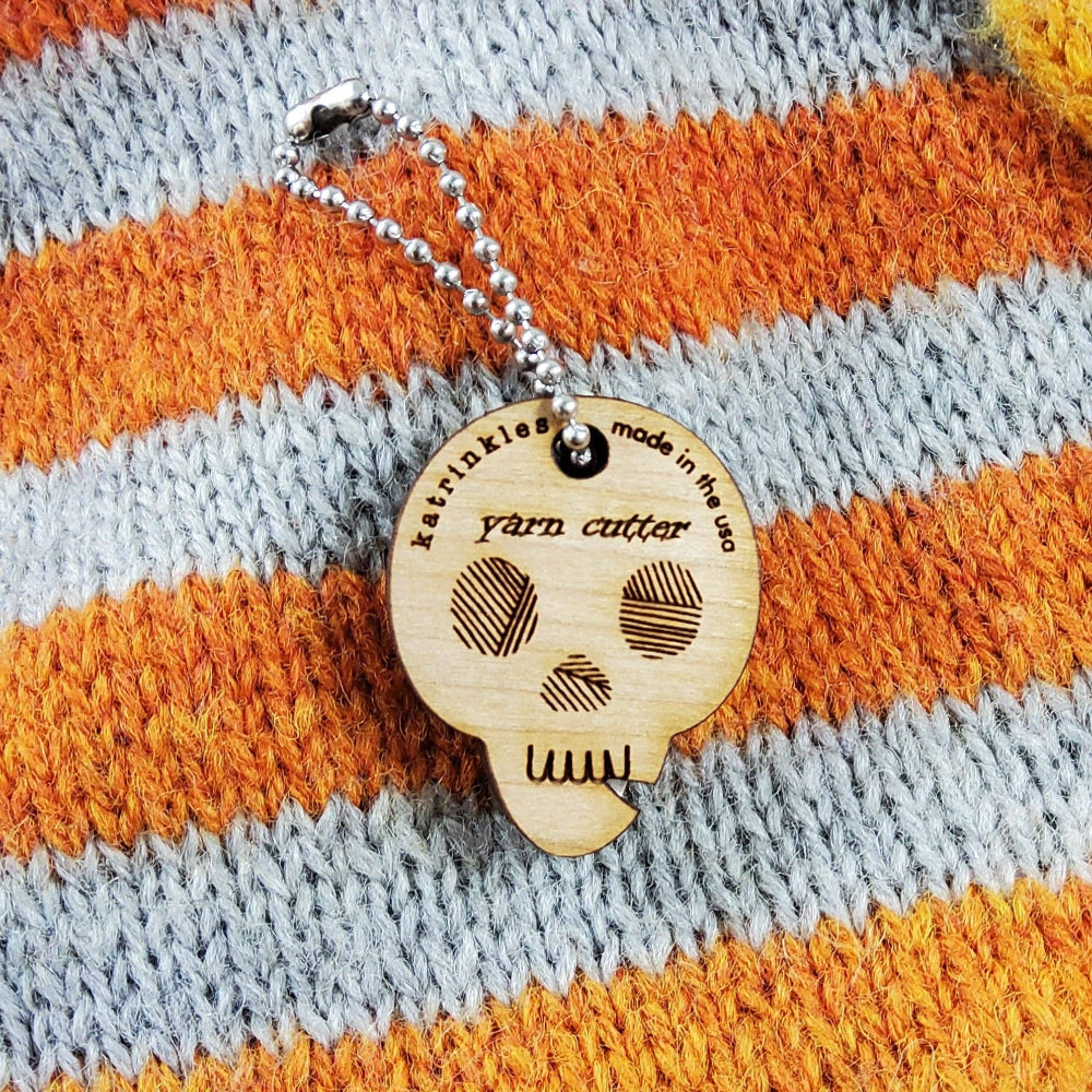 Wood skull yarn cutter on a blue and orange striped knit background