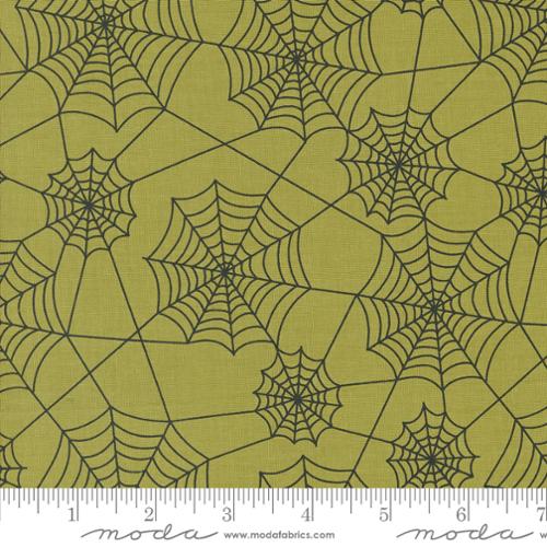 Fabric with spider web pattern on a green background, featuring Moda label.