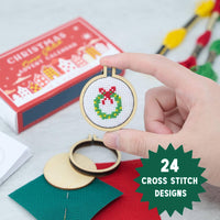 Hand holding a cross-stitched Christmas ornament with an advent calendar in the background