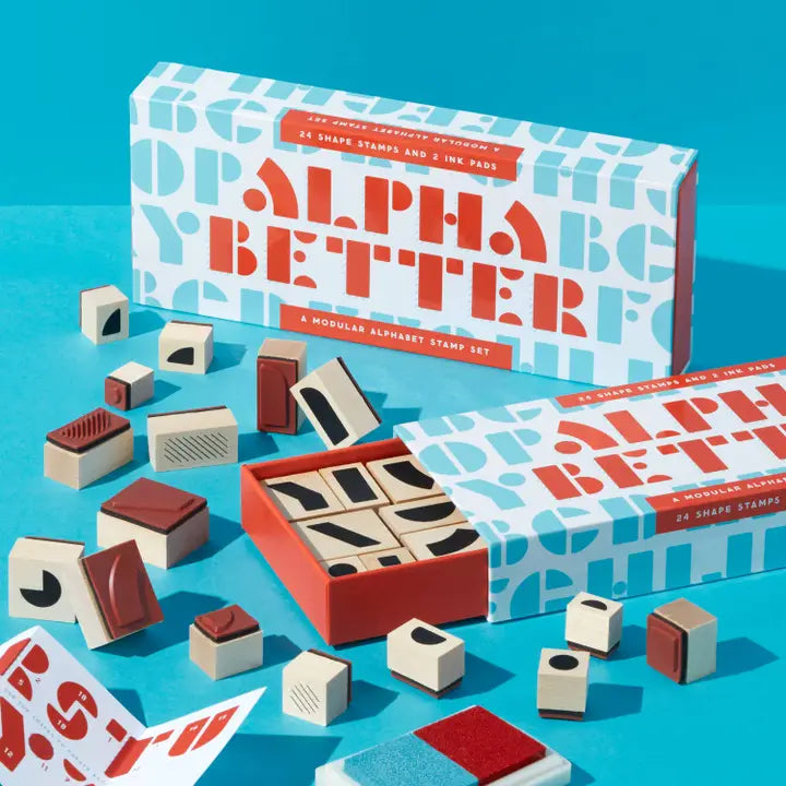 Image of Alpha Better stamp set on blue background showing the stamp set box slid open revealing the wooden stamps with shapes that can be used to make all the letters of the alphabet