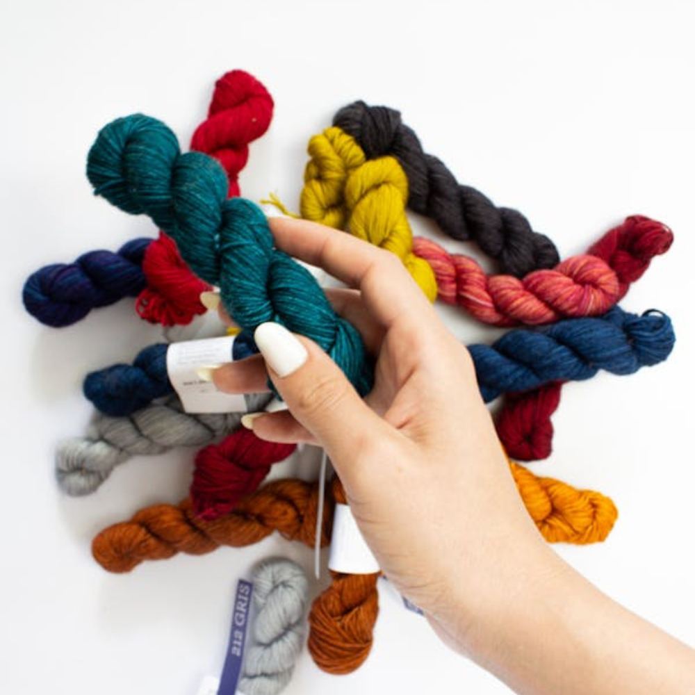 Hand holding colorful yarn skeins against a white background
