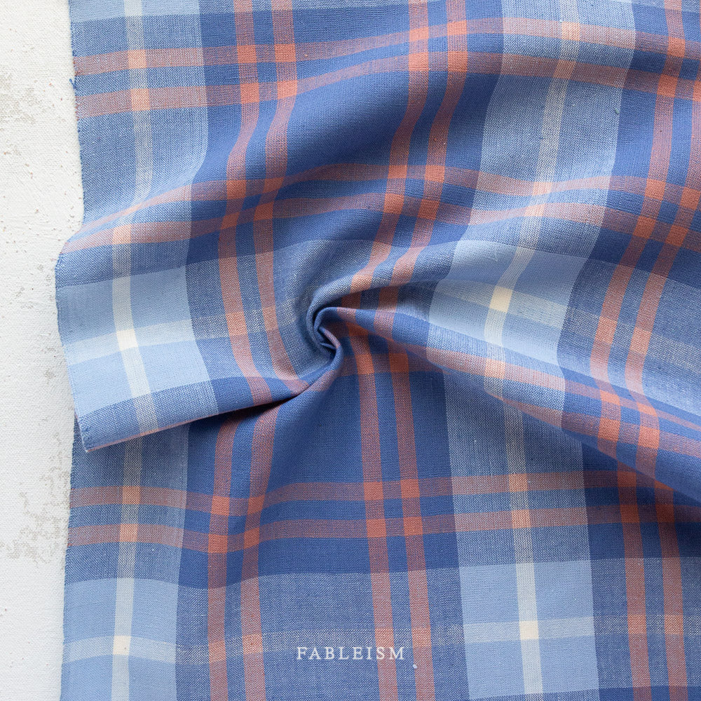 Dark and light blue gingham pattern with orange and white lines interwoven with the word Fableism on the bottom