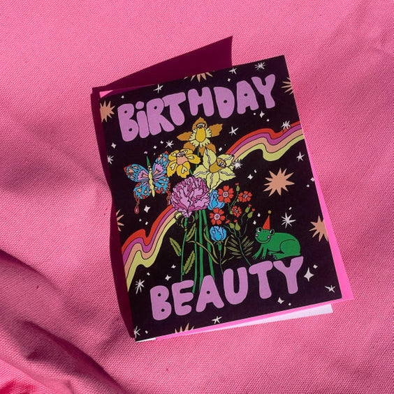 Black card with pink writing 'Birthday Beauty' with flowers and small green frog