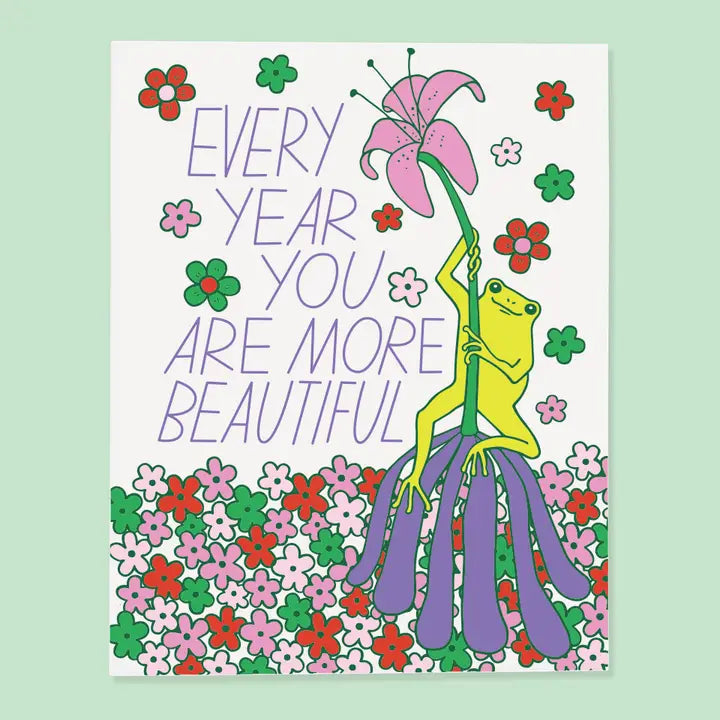 Card with a frog holding a flower and text 'Every year you are more beautiful' on a light green background.
