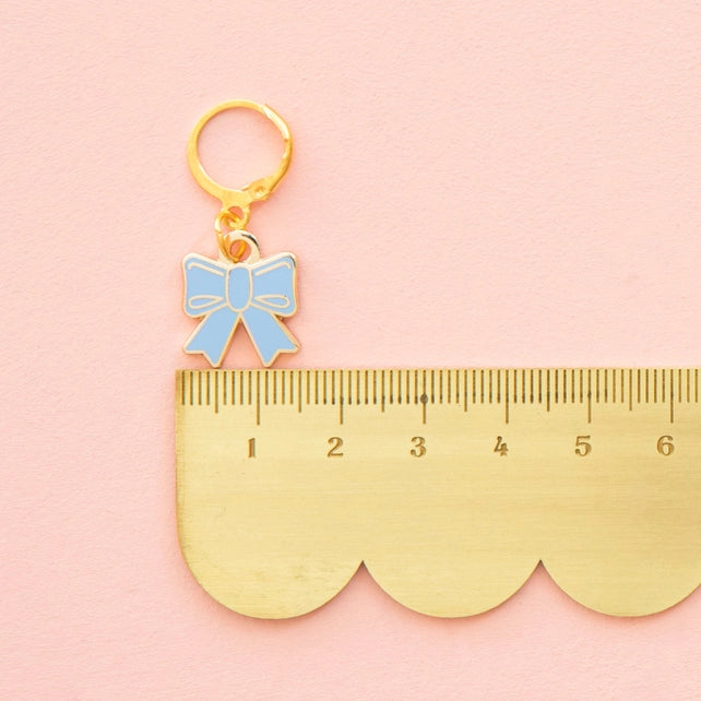 Gold bow-shaped charm on a gold ruler against a pink background
