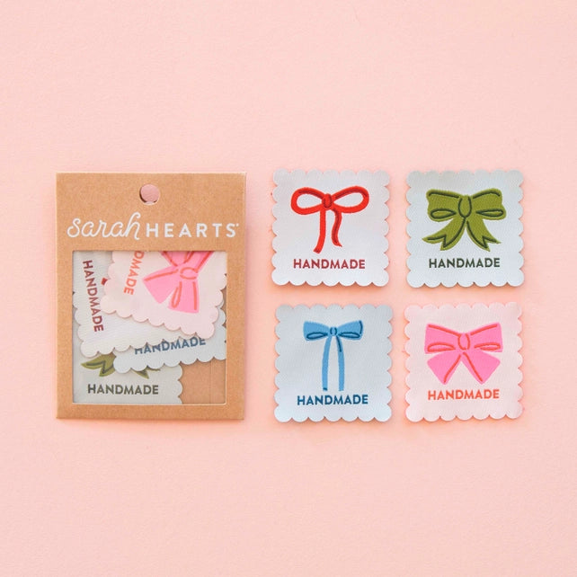 Packaging of 'sarah HEARTS' handmade labels with colorful bows on a pink background