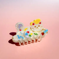 Cat-shaped hair clip with colorful designs on a pink background
