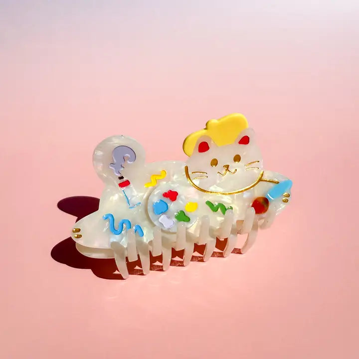 Cat-shaped hair clip with colorful designs on a pink background