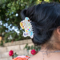 Person with colorful hair clip in dark hair, blurred greenery in the background