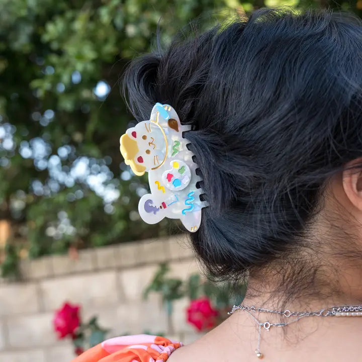Person with colorful hair clip in dark hair, blurred greenery in the background