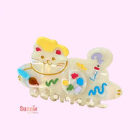 Colorful cat-themed hair clip with cartoon designs on a light pink background