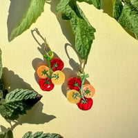 Tomato-themed earrings on a yellow background with green leaves