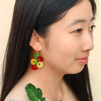 Close-up of a person wearing cherry tomato earrings with a neutral background