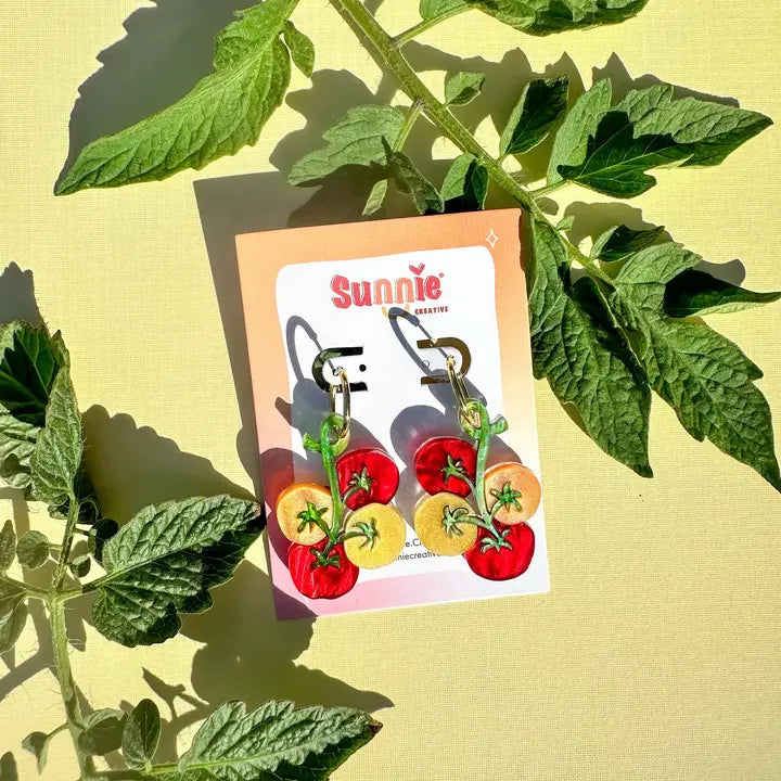 Cherry tomato earrings on a card with green leaves in the background