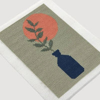 Decorative needlepoint with a blue vase, red sun, and green leaves on a beige background