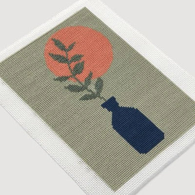Decorative needlepoint with a blue vase, red sun, and green leaves on a beige background