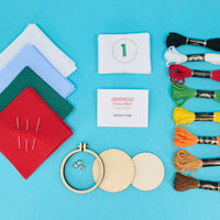 Embroidery kit with fabric, threads, hoop, and needles on a blue background