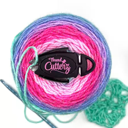 Thread Cutterz tool on a ball of yarn with a crochet hook and crocheted piece in the background.
