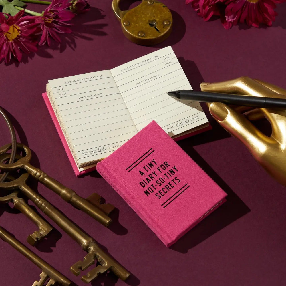 Pink diary with a gold lock, pen, and keys on a purple background