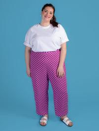 Woman wearing a white top and purple checkered pants against a blue background