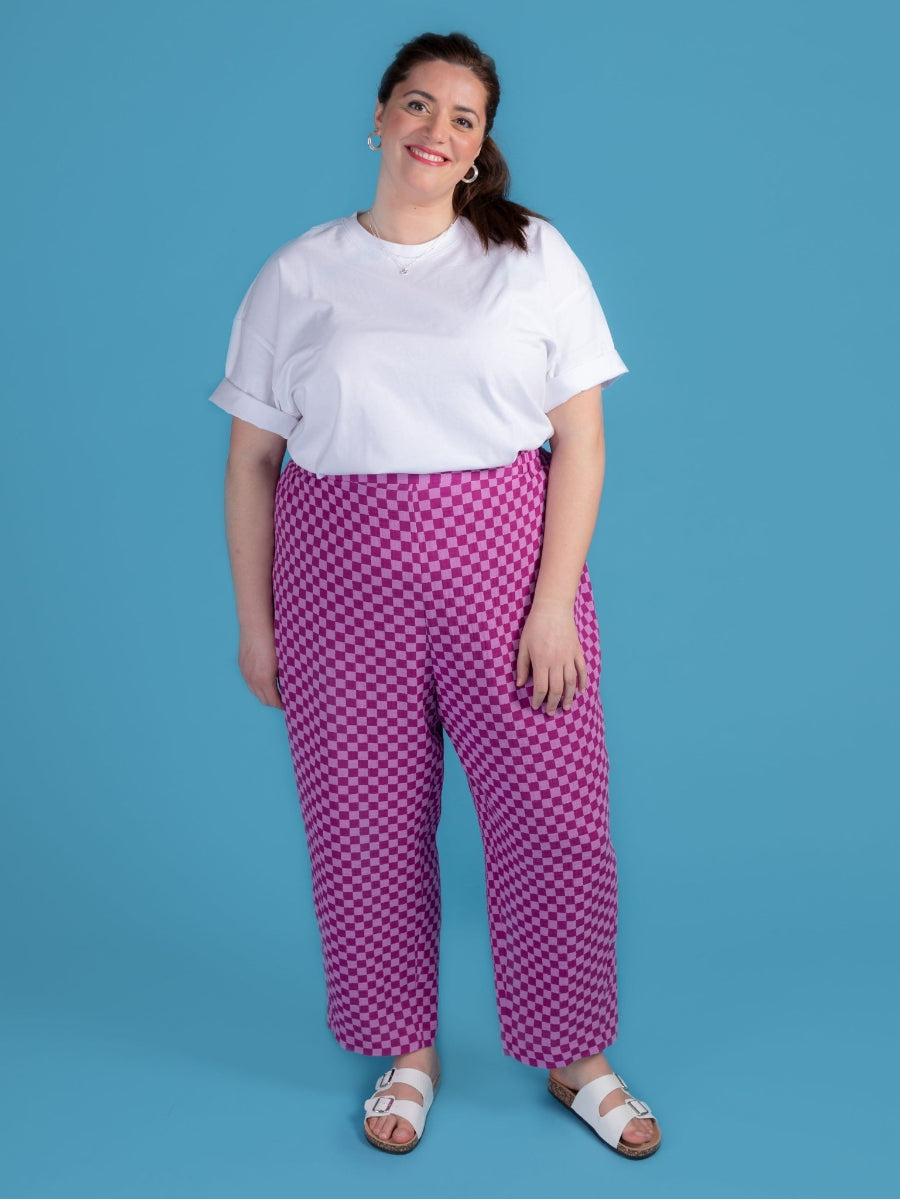 Woman wearing a white top and purple checkered pants against a blue background