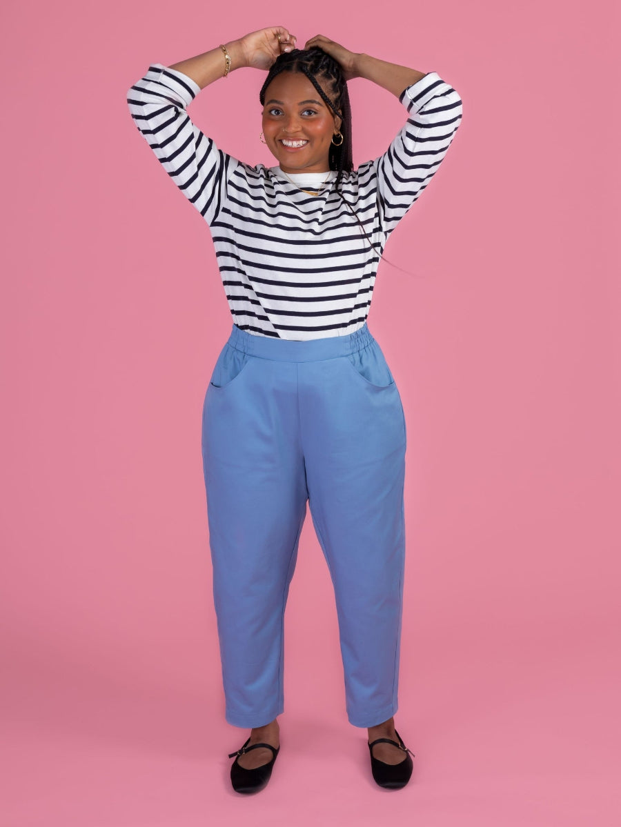 Person wearing a striped shirt and blue pants on a pink background