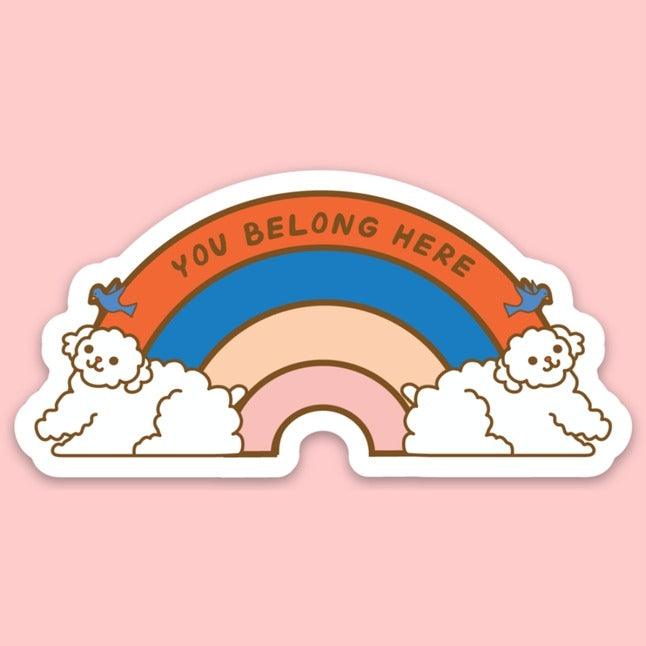 Two white poodles and birds on either side of a red/blue/pink rainbow and the words "You belong here" on top.