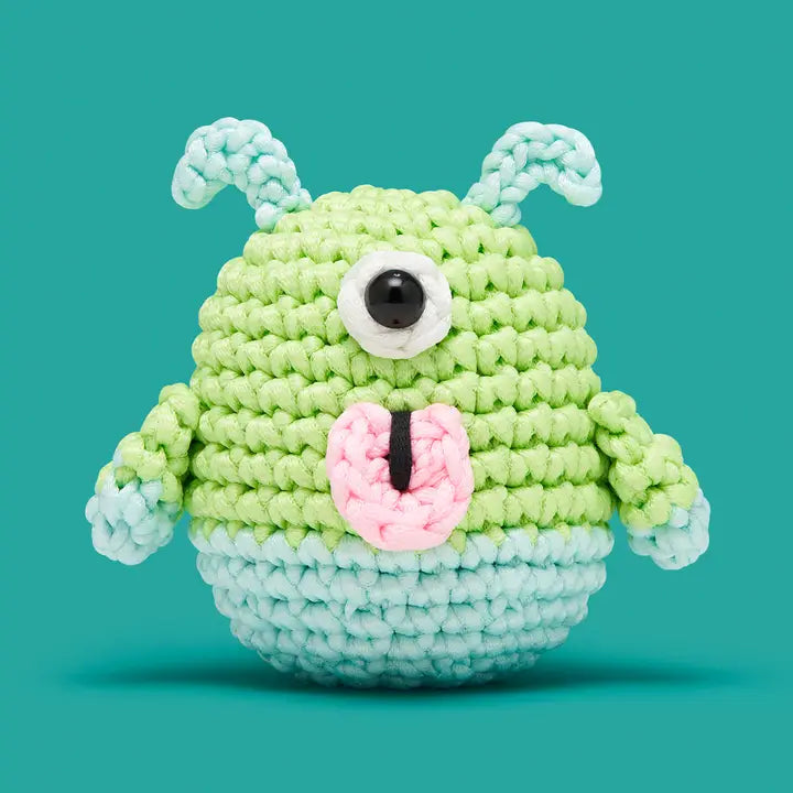 Crocheted green and blue creature with a single eye on a teal background