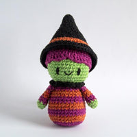A crocheted witch with green skin, a black hat, and colorful dress, amde from the Wicked Witch Crochet Kit from Hoooked