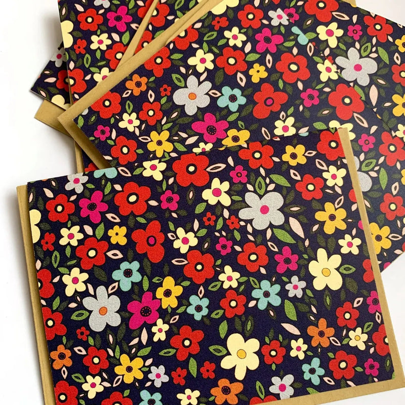 Navy blue background with pink, red, yellow, blue, and silver flowers scattered in a repeating print.