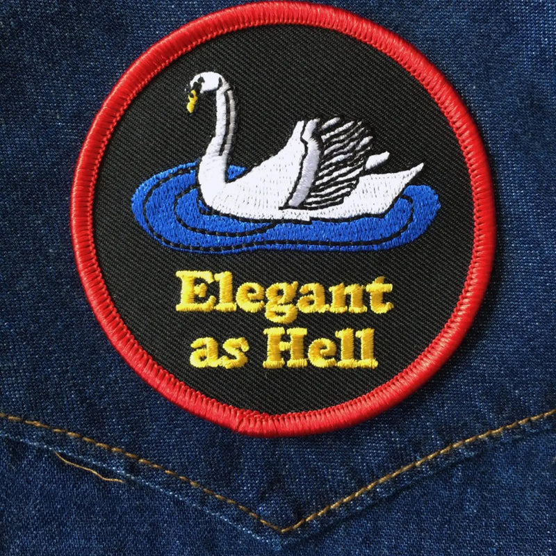 Black patch with red boarder, a white swan, and yellow lettering saying "elegant as hell"