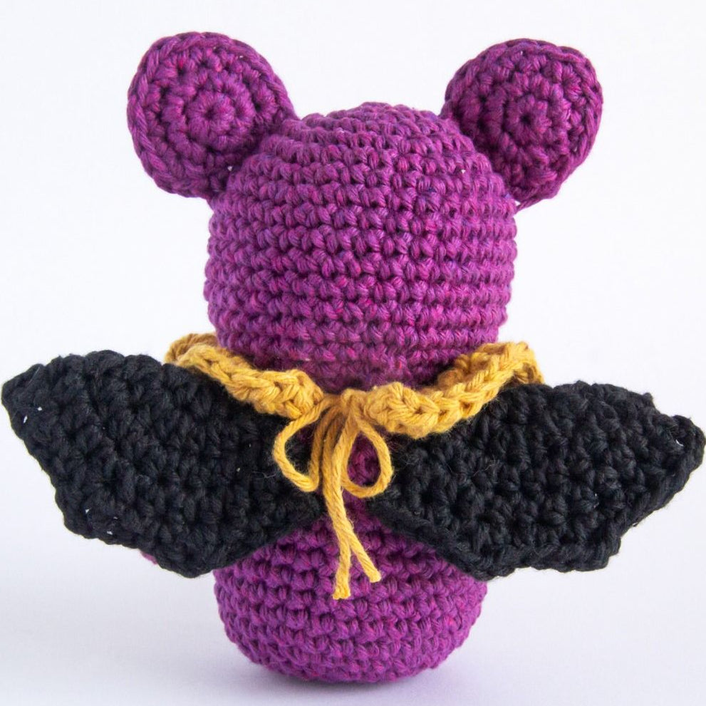 Crocheted purple character with black wings and yellow collar on a white background