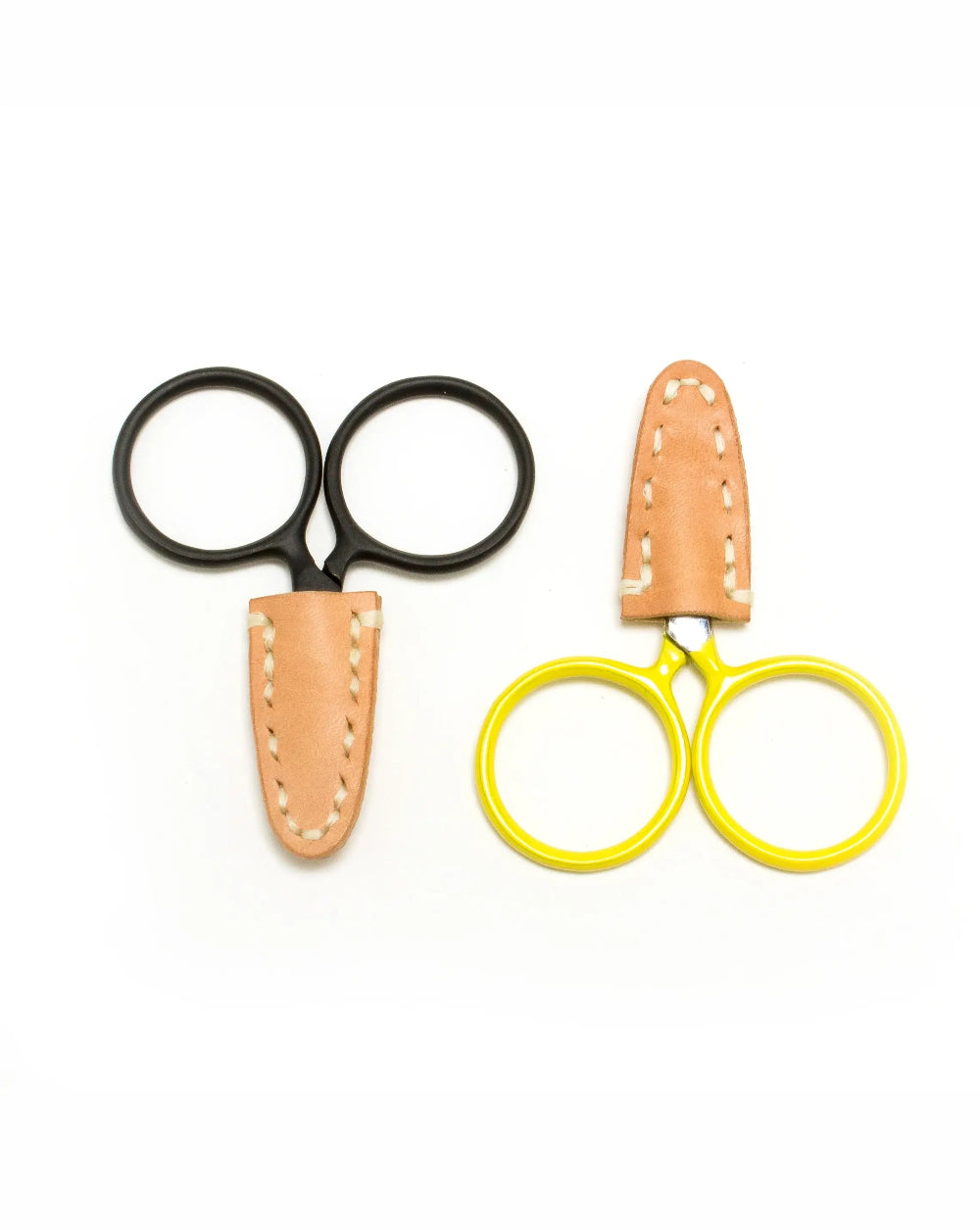 Two pairs of scissors with leather sheaths on a white background