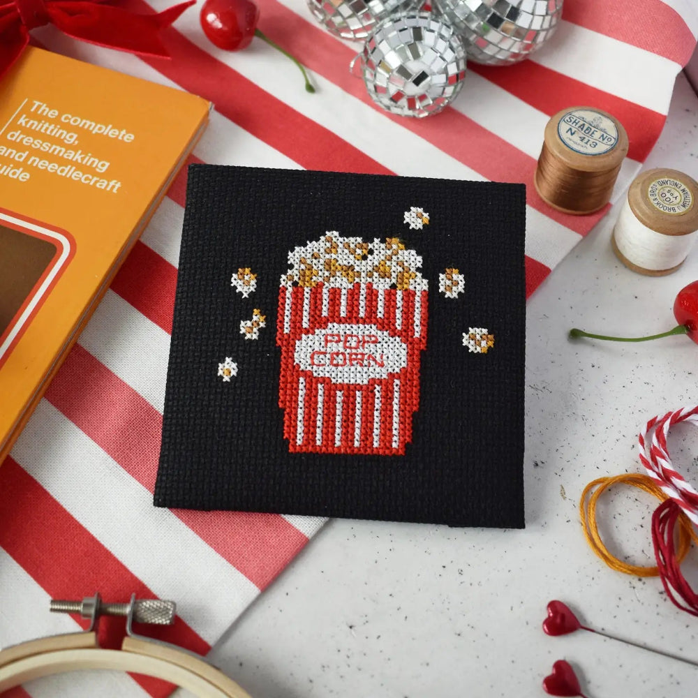 Cross-stitched popcorn design on black fabric with cross stitch supplies around