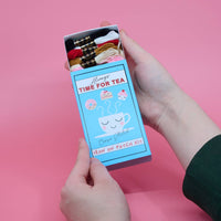Hand holding a box of 'Always Time for Tea' iron on patch kit against a pink background