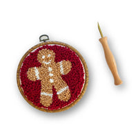 Embroidery hoop with gingerbread man design and a needle on a white background