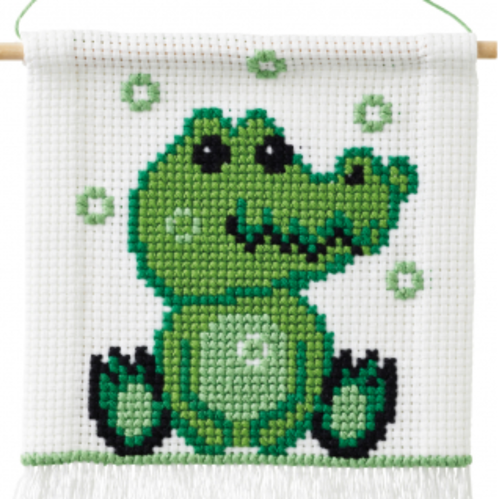 Green crocodile cross stitch on white background with wooden rod on top and white fringe on the bottom.