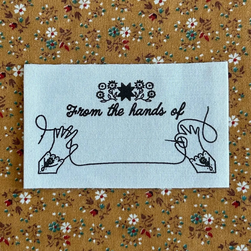Embroidered label with 'From the hands of' text on a floral fabric background