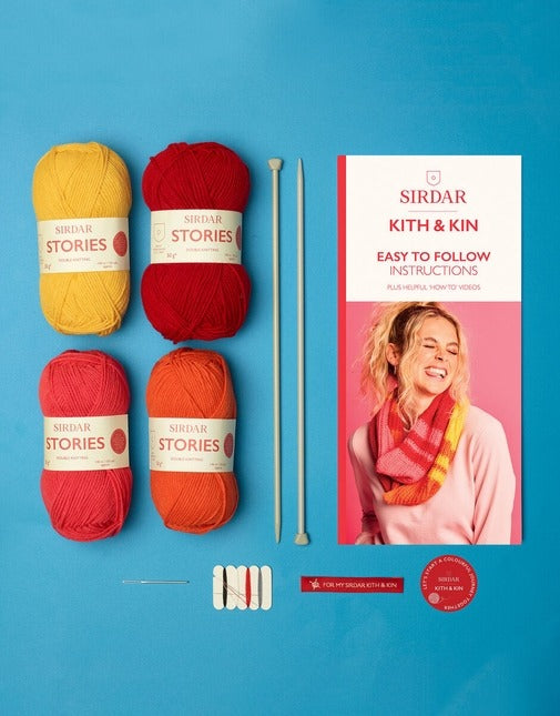 Yarn balls, knitting needles, and a Sirdar Kith & Kin book on a blue background