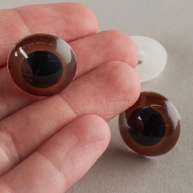 Two brown glass eyes held between fingers on a neutral background