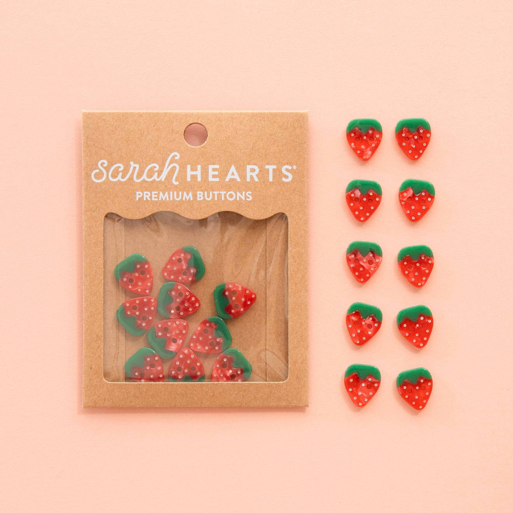 Packaged strawberry-shaped buttons with 'Sarah Hearts' branding on a pink background