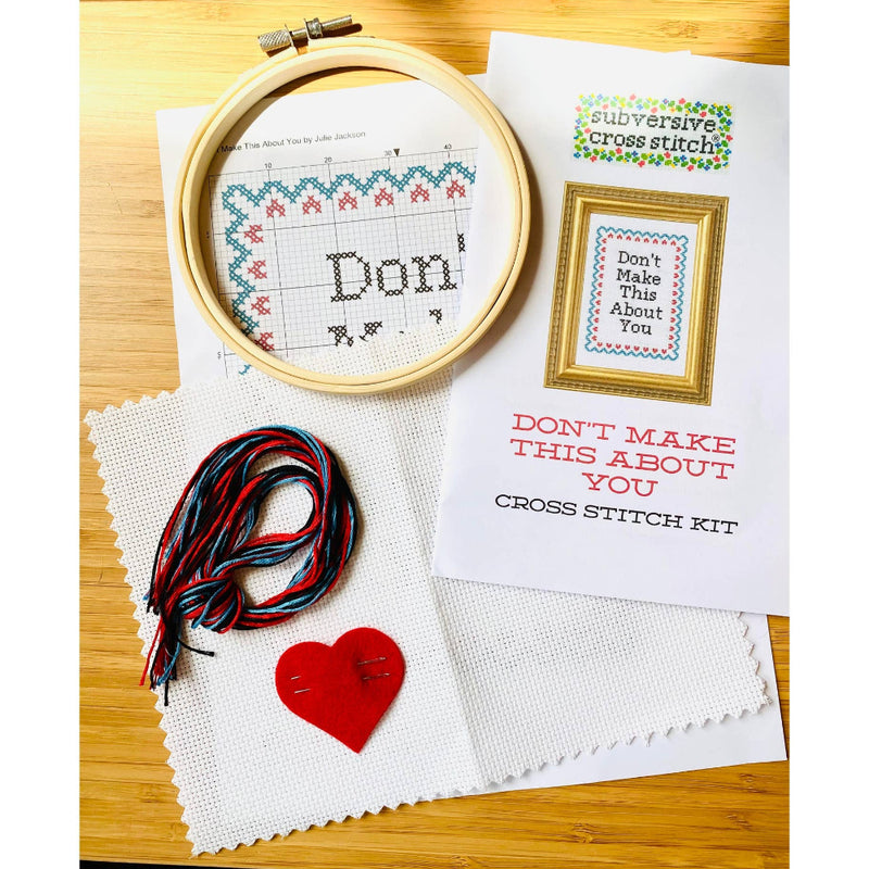 Cross stitch kit with hoop, thread, red heart, and printed instructions on a wooden surface.