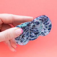 Hand holding a blue and white patterned yarn skein hair claw against a pink background
