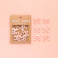 Packaged pink flower buttons with 'sarah HEARTS' branding on a pink background