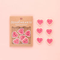 Packaging of pink heart-shaped buttons with 'sarahHEARTS' branding on a pink background.