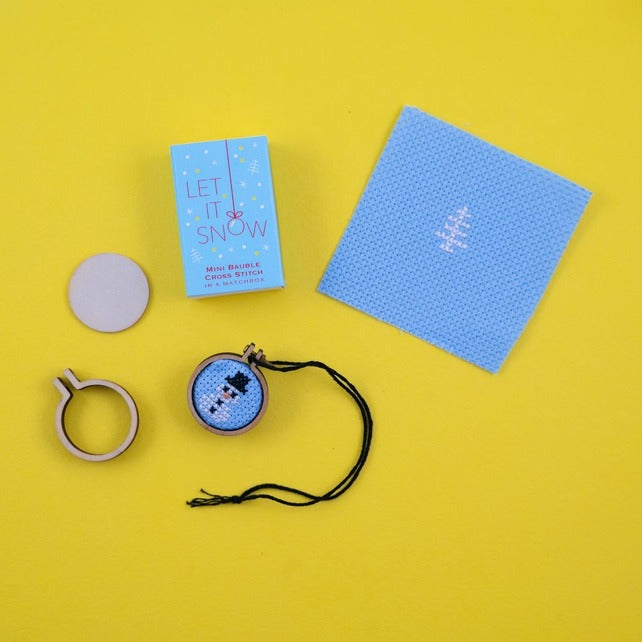 Cross-stitch kit with a completed snowman design on blue aida cloth, hoop, and thread on a yellow background