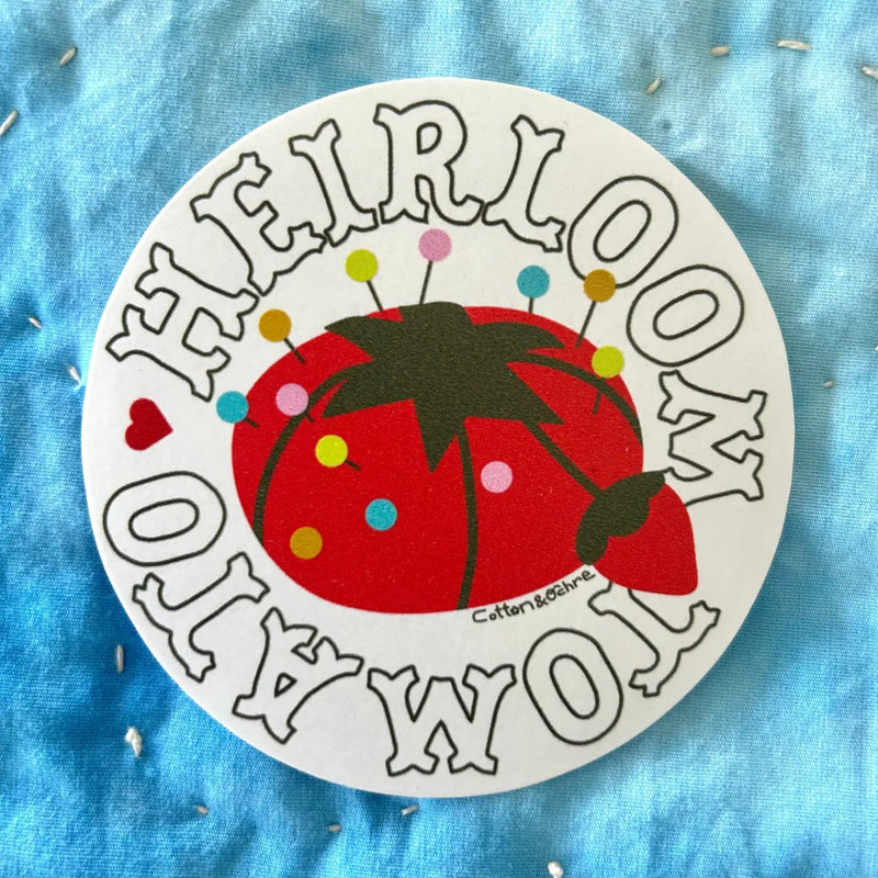 Circular sticker with a red tomato design and text on a blue fabric background
