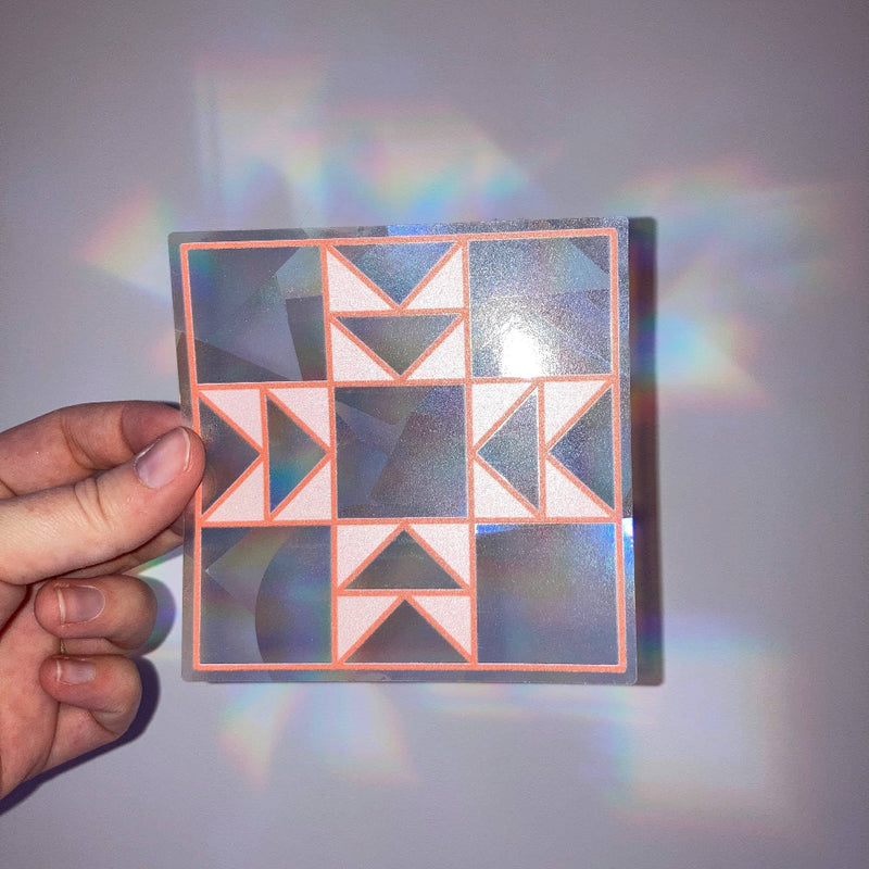 Hand holding a geometric patterned sticker with reflective rainbow
