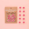 Heart-shaped buttons with 'sarahHEARTS' packaging on a pink background